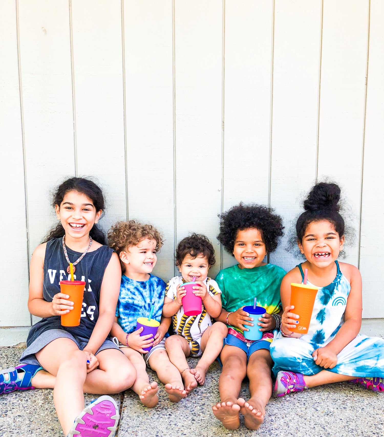 5 children sitting on the ground, smiling, and holding a reusable silicone tumbler 